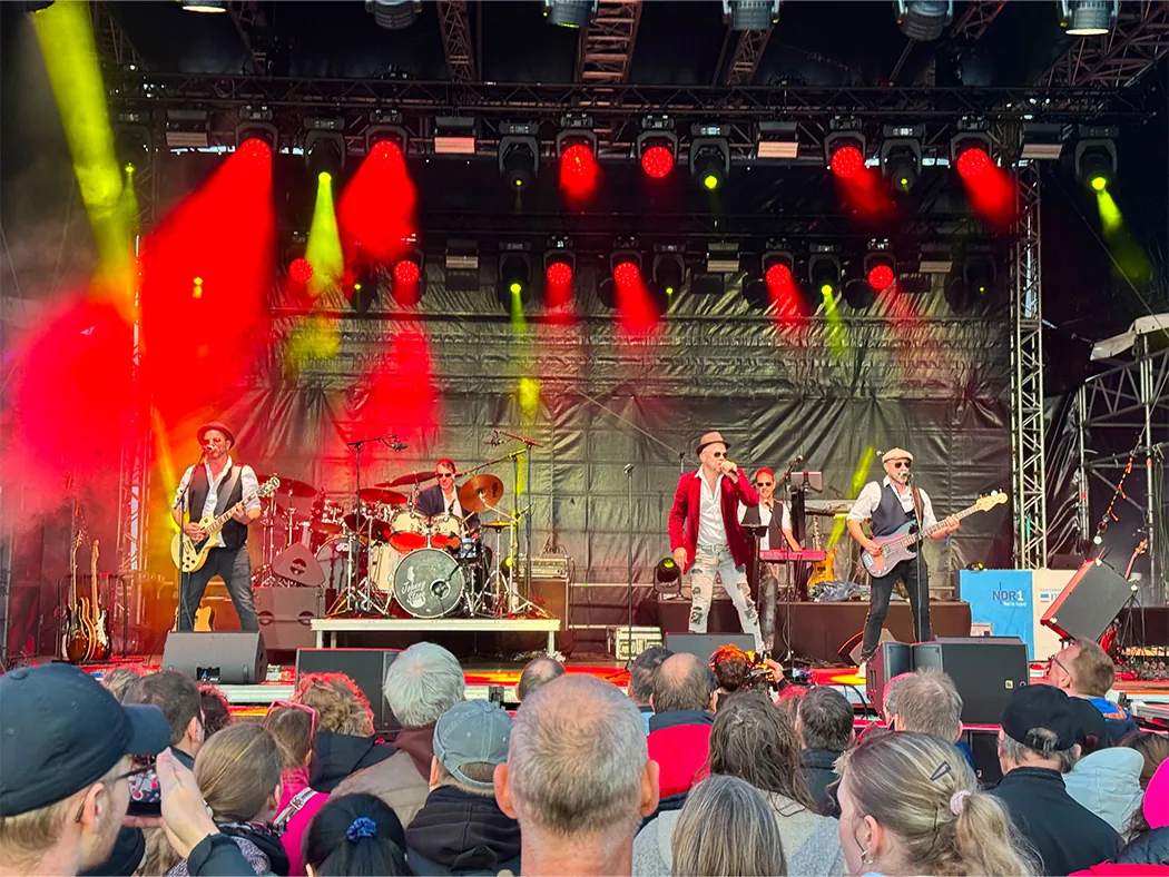 Johnny Stone spielt auf einer großen Festivalbühne unter roten und gelben Scheinwerfern, davor eine Publikumsmenge.