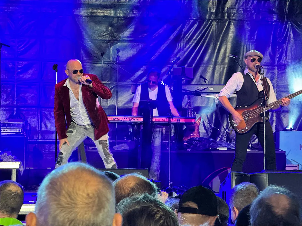 Johnny Stone in blauem Licht: der Sänger im roten Samtsakko und der Bassist mit Schiebermütze, dahinter der Keyboarder.
