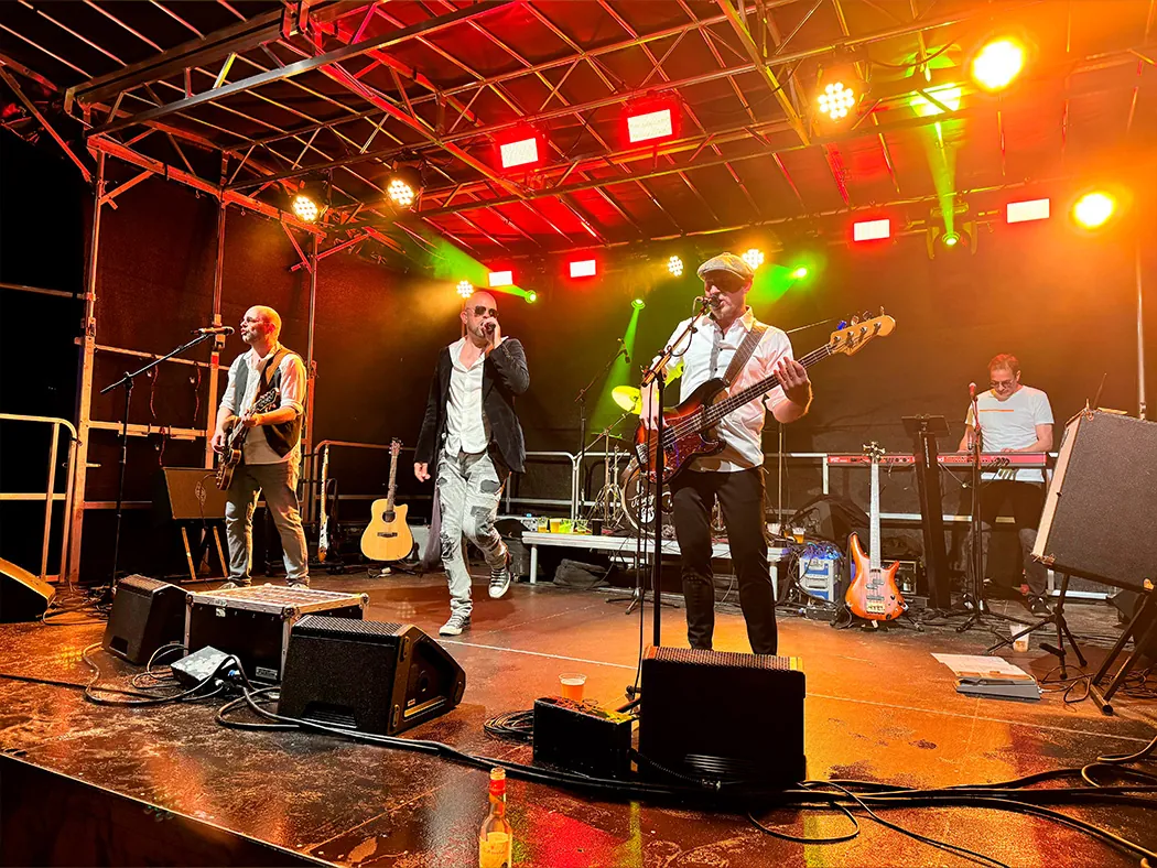 Johnny Stone auf einer Bühne mit roten und gelben Scheinwerfern: Gitarrist, Sänger, Bassist und Keyboarder bei der Show.
